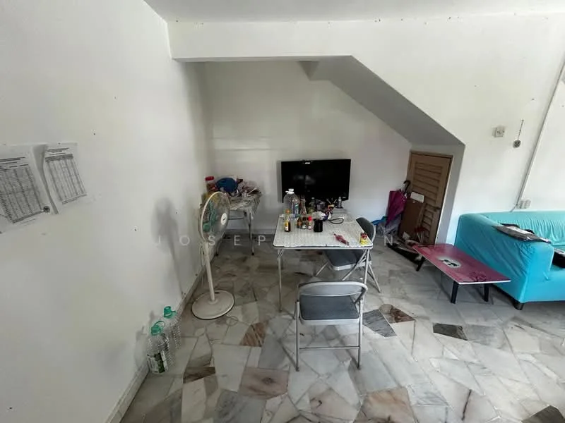 Living features: white painted walls, marble flooring, sofa in turquoise, wall-mounted TV, folding table, plastic chairs, standing fan, various bottles and items on table, storage cabinet, corner with sloped ceiling.