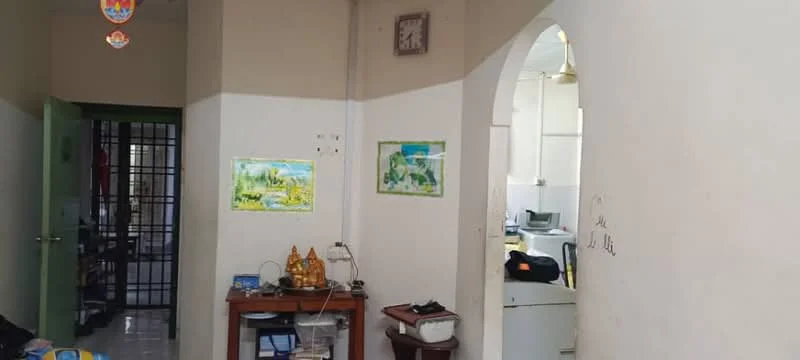 Room features: white painted walls, glossy tile flooring, wooden console table, framed artwork on walls, wall clock, doorway leading to another room, visible kitchen area in background, ceiling fan.