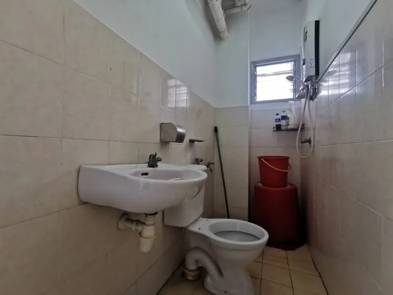 Bathroom features: white ceramic toilet, white ceramic sink, chrome faucet, shower head, wall-mounted shower mixer, tile flooring, light beige wall tiles, window for natural light, red storage container.