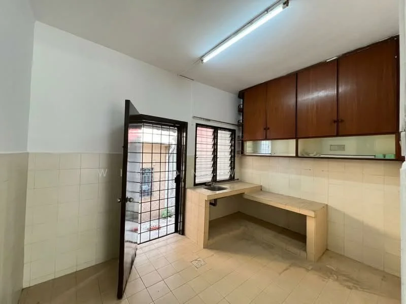 Kitchen features: white tiled walls, light beige tiled flooring, wood cabinetry with brown finish, single-bowl stainless-steel sink, countertop with built-in workspace, window with security grille, door leading outside, fluorescent ceiling light.