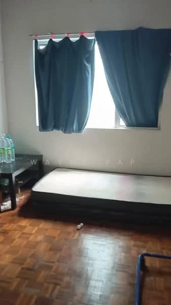 Room features: wooden flooring, single bed frame, mattress on bed frame, blue curtains, window with natural light, small black table, bottled water on table, empty space on floor; style: minimalist.