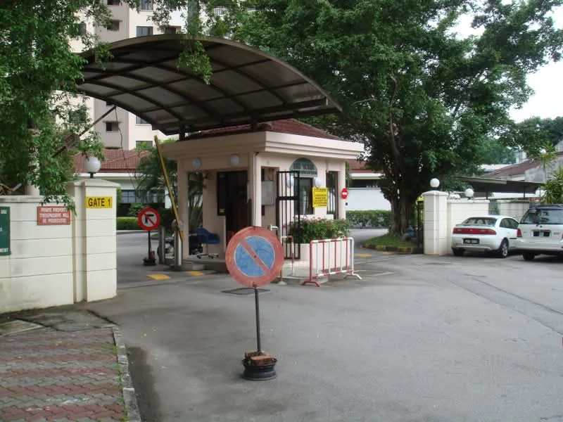 Exterior type: main entrance gate; features: guard house at entrance, covered drop-off area, paved driveway, traffic sign indicating no parking, surrounded by mature trees, security barriers, visible parking area, street lighting, signage for gate, white painted walls; style: modern.