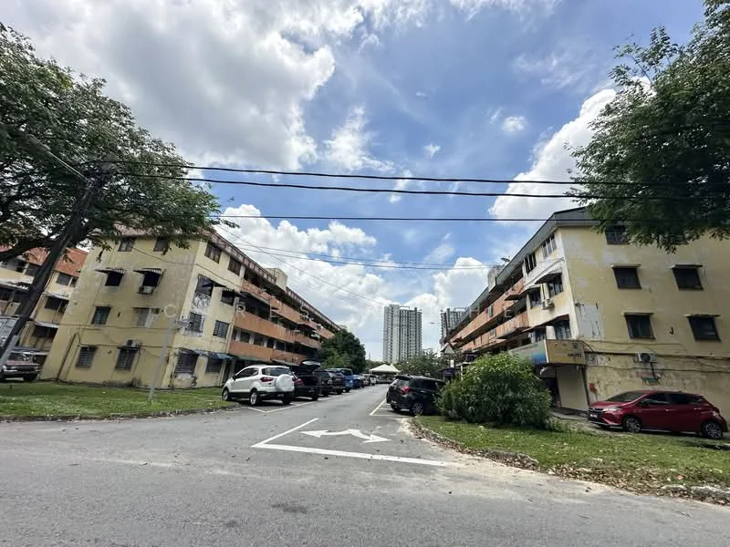 Exterior type: low-rise apartment block; features: two-storey building, balconies on upper floor, parking spaces visible, surrounded by greenery, cloudy sky, roadway with directional markings, adjacent high-rise buildings; style: traditional.