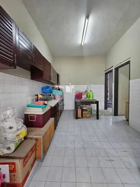 Kitchen features: white tiled flooring, white tiled walls, dark wooden cabinetry, double-basin sink, countertop with storage underneath, refrigerator, cooler box, plastic storage containers, rolls of paper towels, multiple bottles on countertop, open shelving, doorway leading to another room.