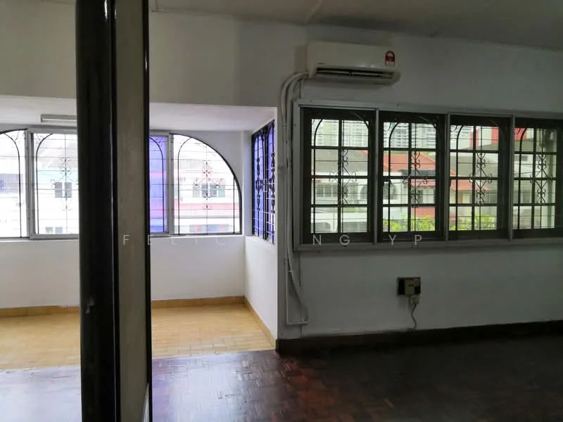 Room features: wooden flooring, white painted walls, large windows with metal grills, air conditioning unit, natural light from windows, corner room layout, visible electrical outlets, partitioned space.