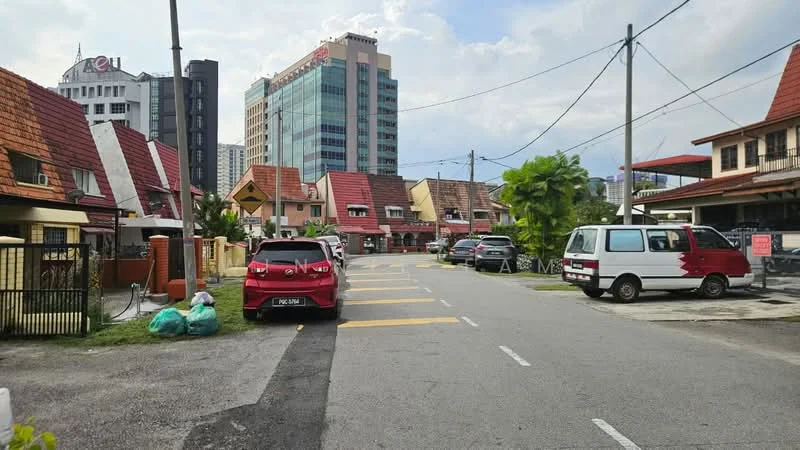 Exterior type: linked terrace house; features: red tiled roof, cream painted facade, two-storey houses, paved driveway, manicured lawn, surrounded by mature greenery, urban context with high-rise buildings in background, multiple parked cars, street lighting, sidewalk; style: modern.