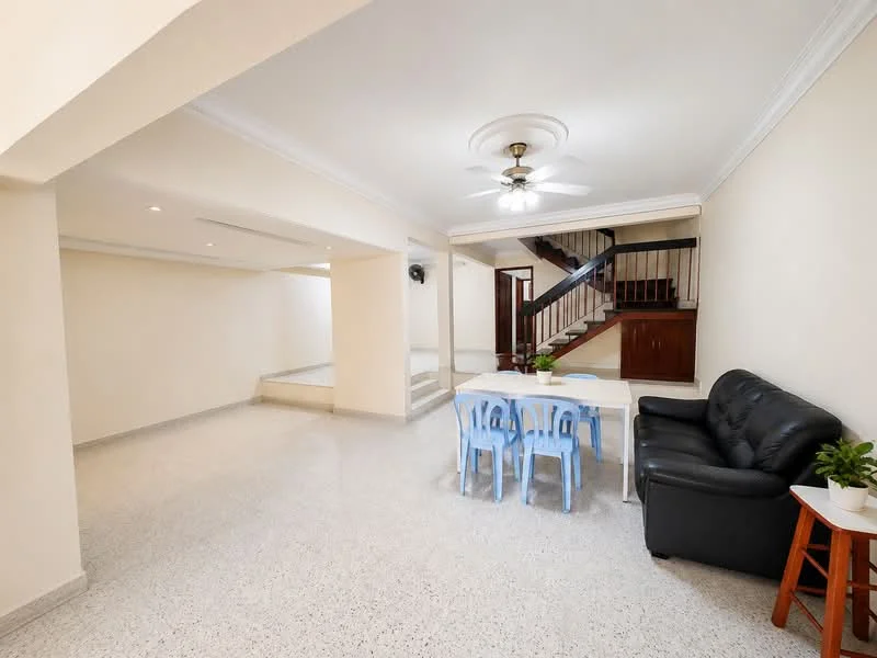 Living features: light grey terrazzo flooring, cream painted walls, 5-blade ceiling fan with light, sofa in black leather, dining table with blue plastic chairs, staircase with wooden railing, recessed lighting, crown moulding; style: modern.