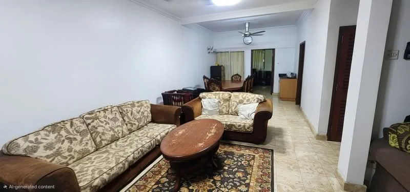 Living features: 3-seater fabric sofa with floral pattern, 2-seater fabric sofa in brown, round wooden coffee table, area rug with intricate pattern, cream painted walls, tile flooring, ceiling fan, wall-mounted air conditioning unit, decorative wall clock, dining area visible in background, wooden dining chairs, wooden dining table; style: traditional.