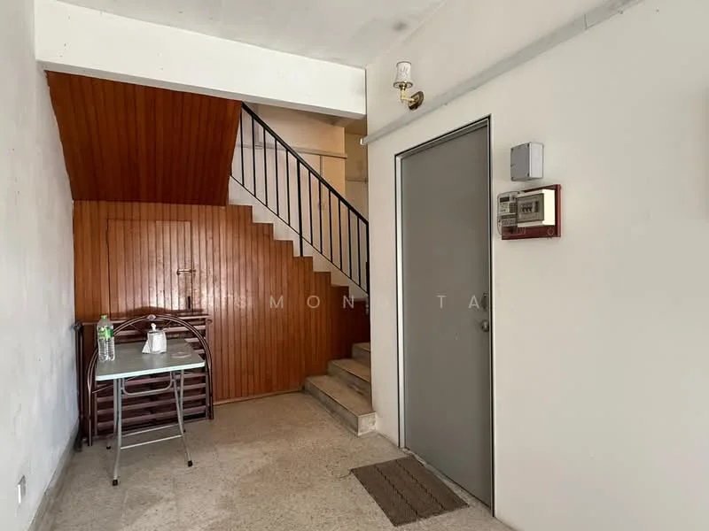 Room features: staircase with wooden treads, metal railing, cream painted walls, concrete flooring, wood paneling on wall, door with grey finish, wall-mounted intercom, small table with chairs, water dispenser, doormat; style: minimalist.