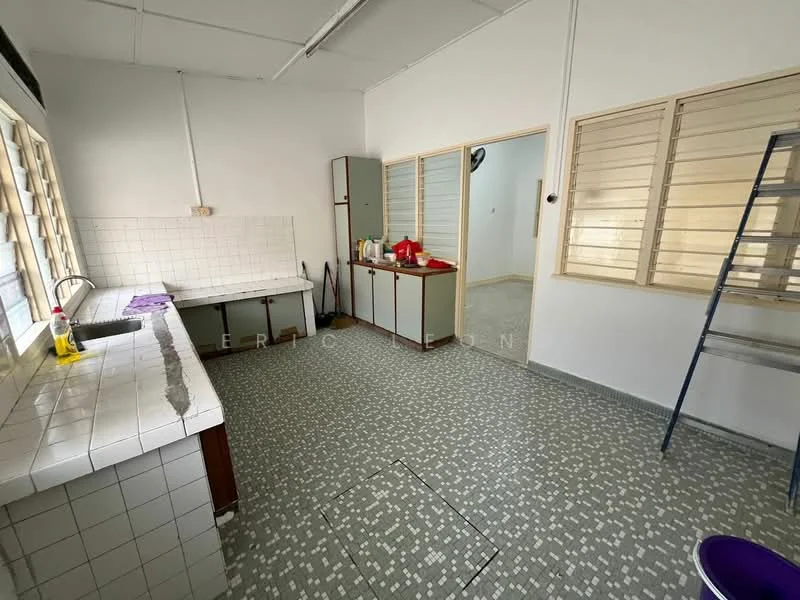 Kitchen features: white tiled walls, grey patterned floor tiles, single-bowl stainless-steel sink, chrome pull-down faucet, white countertop, wooden cabinetry, open shelving, window with horizontal slats, kitchen island, cleaning supplies on countertop.