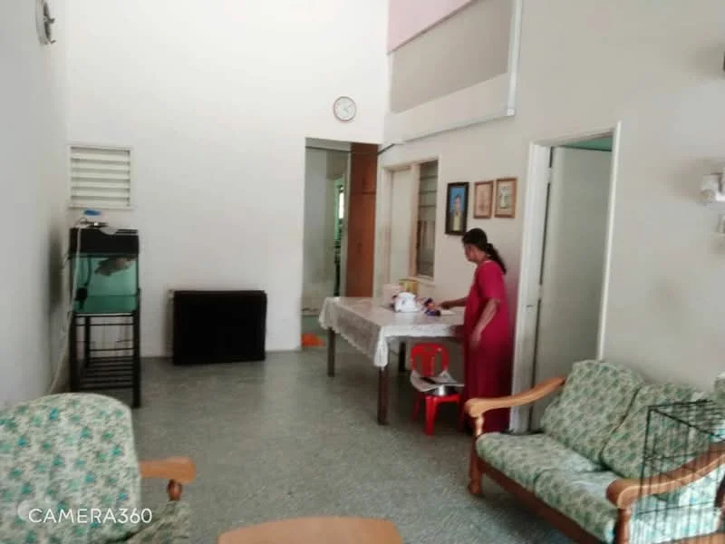 Living features: green floral-patterned fabric sofa, 2-seater fabric sofa, wooden coffee table, tile flooring, white painted walls, ceiling fan, wall-mounted clock, open doorway to adjacent room, window with no visible treatment, decorative wall art, dining table with tablecloth, red plastic chair.
