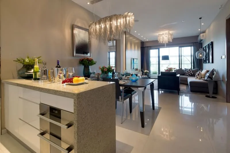 Dining features: marble countertop, white cabinetry, glass dining table, upholstered dining chairs, decorative vase with flowers, wine bottles, fruit bowl, table setting with plates and cutlery, chandelier lighting, recessed downlights, floor-to-ceiling windows, grey accent wall, polished tile flooring; style: modern; view: city. Living features: 3-seater fabric sofa in grey, decorative cushions, coffee table, wall-mounted TV, entertainment unit, area rug, floor-to-ceiling windows, light curtains, recessed downlights, decorative artwork, open layout, polished tile flooring; style: modern; view: city.
