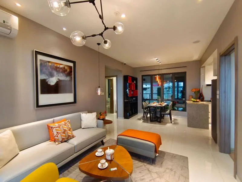 Living features: grey painted walls, white ceiling with recessed downlights, 3-seater fabric sofa in light grey, orange accent chair, wooden coffee table with curved edges, decorative cushions, framed artwork on wall, pendant light fixture, floor-to-ceiling windows, sliding glass door, area rug with geometric pattern, air conditioning unit mounted on wall; style: modern; view: garden. Dining features: dining table for six, black dining chairs, decorative centerpiece, open kitchen area visible, red shelving unit, kitchen island with countertop; style: modern; view: garden.