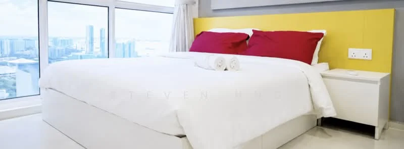 Bedroom features: king-size bed with white bedding, yellow headboard, red decorative pillows, white bedside table, city skyline view from window, floor-to-ceiling windows, light-colored flooring, curtains, towels rolled on the bed; style: modern; view: city.