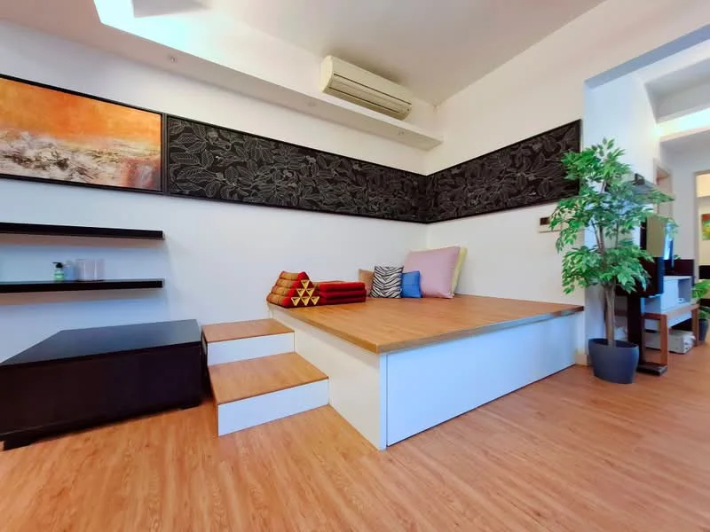 Living features: wooden flooring, white painted walls, black feature wall with floral design, built-in shelving unit, step-up platform, decorative cushions in various colors, potted plant, air conditioning unit; style: modern.