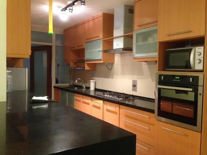 Kitchen features: wood cabinetry in light brown, black granite countertop, stainless-steel built-in oven, stainless-steel microwave, 4-burner gas hob, stainless-steel range hood, double-bowl stainless-steel sink, chrome pull-down faucet, glass-front upper cabinets, recessed downlights, tile backsplash, open shelving, floor-to-ceiling windows, kitchen island with seating, ceramic tile flooring; style: modern.