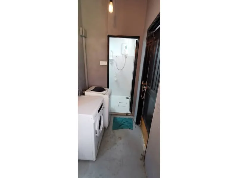 Laundry features: front-load washing machine, top-load washing machine, white walls, grey flooring, single light pendant, door leading to bathroom, towel on floor.