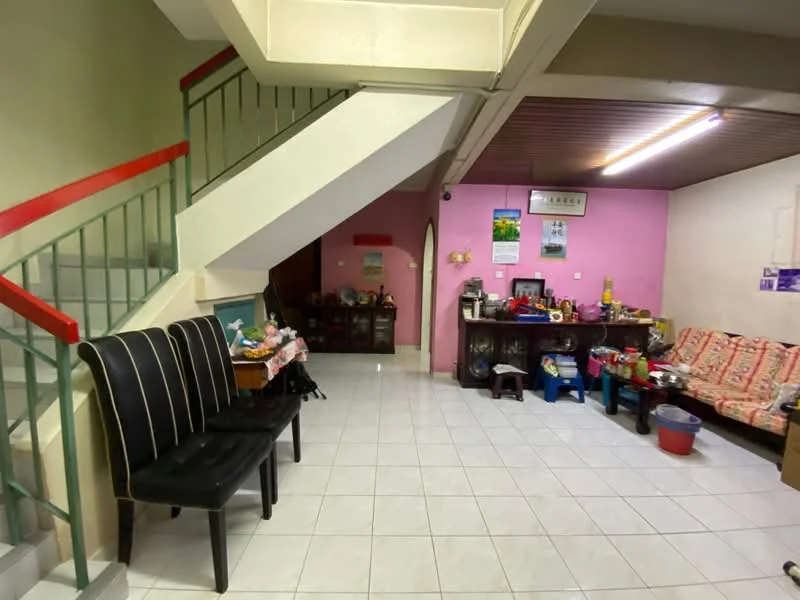 Living features: white tiled flooring, pink painted walls, wooden ceiling, staircase with green railing, black upholstered chairs, wooden side table, sofa with floral upholstery, decorative wall art, shelves with various items, light fixture on ceiling.