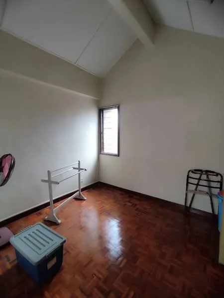 Room features: wooden flooring, white painted walls, slanted ceiling, single window, clothes drying rack, folding chair, storage box.