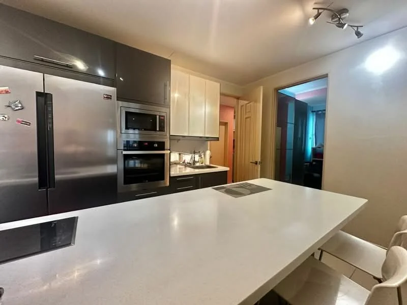 Kitchen features: stainless-steel fridge, built-in oven, microwave, white quartz countertop, kitchen island with seating, dark cabinetry, light cabinetry, recessed lighting, induction cooktop, splashback, modern bar stools; style: modern.