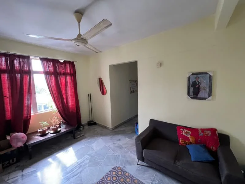 Living features: grey fabric sofa, red decorative cushion, ceiling fan, large window with sheer red curtains, marble flooring, wall-mounted mirror, decorative wall art, plant pots on window sill, light yellow painted walls; style: minimalist; view: garden. Room features: light yellow painted walls, doorway leading to another room.