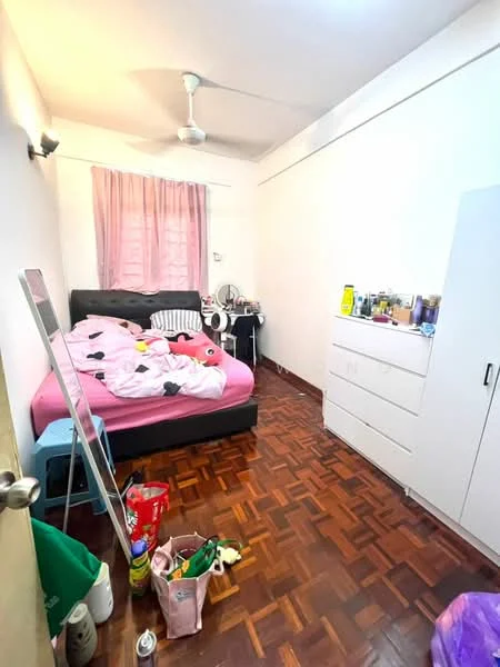 Bedroom features: pink bed with bedding, black headboard, light pink curtains, wooden parquet flooring, ceiling fan, white dresser with drawers, mirror, various personal items on dresser, plastic chair, laundry basket, stuffed toys on floor.