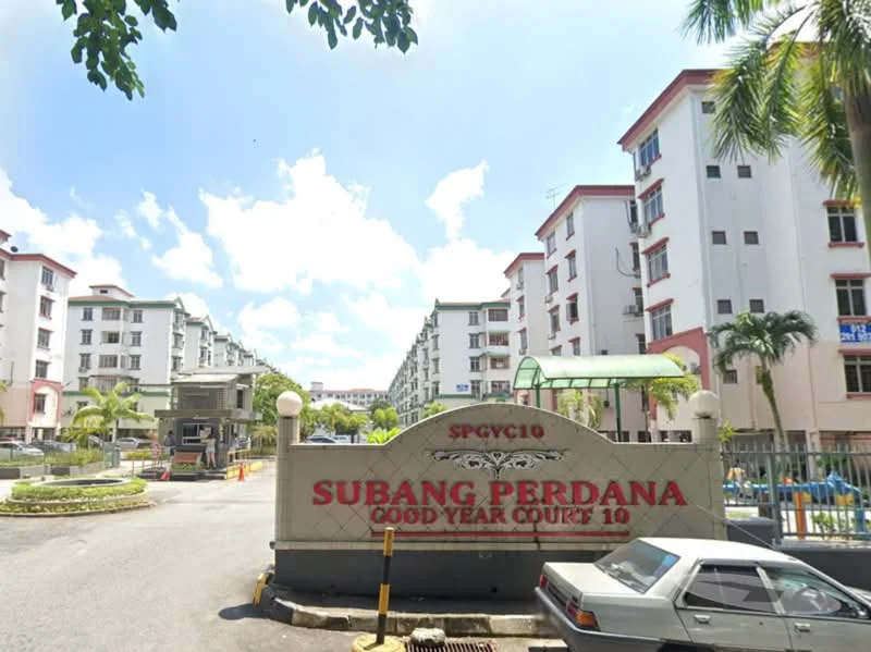 Exterior type: low-rise apartment block; features: white painted facade, red brick accents, manicured landscaping, palm trees, guard house at entrance, gated entry, driveway with interlocking pavers, signage with property name, surrounded by greenery, multiple storeys, parking area; style: modern.
