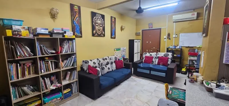 Living features: 2 black fabric sofas with cushions in red and white, bookshelf with multiple shelves filled with books and decorative items, wall-mounted air conditioning unit, wall art featuring a Buddha face, cream painted walls, marble flooring, ceiling fan, small table with various items, whiteboard on the wall, decorative items on shelves; style: contemporary.