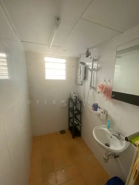 Bathroom features: white tiled walls, yellow ceramic tile flooring, shower with handheld showerhead, wall-mounted mirror, sink with chrome faucet, open shelving unit, window for natural light, toilet paper holder.