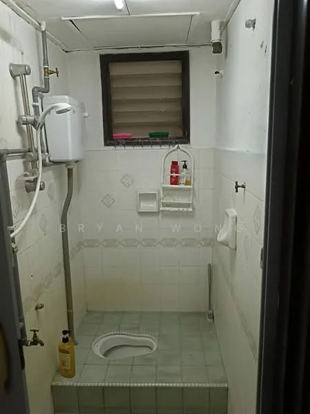 Bathroom features: white tiled walls, grey tiled flooring, squat toilet, shower area with no enclosure, window for ventilation, wall-mounted soap dispenser, shelf for toiletries, exposed plumbing, light fixture on ceiling.