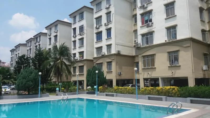 Exterior type: low-rise apartment block; features: swimming pool, landscaped garden with shrubs, palm trees, multiple storeys, balconies on upper floors, air conditioning units visible on facade, parking area visible, light fixtures around pool area; style: modern.