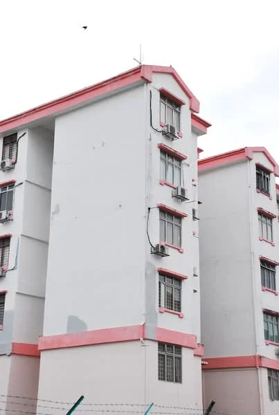 Exterior type: low-rise apartment block; features: white painted facade, pink trim on roof and windows, multiple air conditioning units visible, three-storey building, grid-patterned windows, fenced perimeter; style: modern.