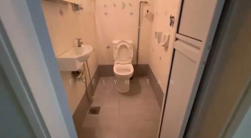Bathroom features: white ceramic toilet, single-sink vanity with chrome faucet, grey floor tiles, white walls with blue decorative tiles, wall-mounted toilet paper holder, built-in cabinet, shower area with drain.