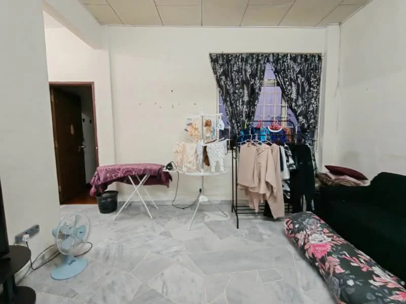 Room features: white painted walls, marble tile flooring, black fabric sofa, folding ironing board, clothes rack with hanging clothes, decorative floral area rug, window with sheer curtains, ceiling fan.