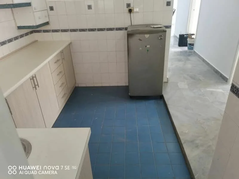Kitchen features: white cabinetry, laminate countertop, stainless-steel fridge, single-bowl stainless-steel sink, chrome pull-down faucet, blue ceramic tile flooring, white tiled walls, grey marble flooring, wall-mounted electrical outlet, backsplash with decorative tiles; style: modern.