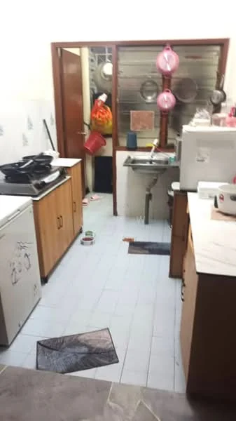 Kitchen features: white tiled walls, light blue tiled flooring, wood cabinetry with brown finish, black countertop, double-bowl stainless-steel sink, chrome faucet, freestanding gas stove with 4 burners, refrigerator, kitchen mats, hanging pots and pans, open door leading to another room.