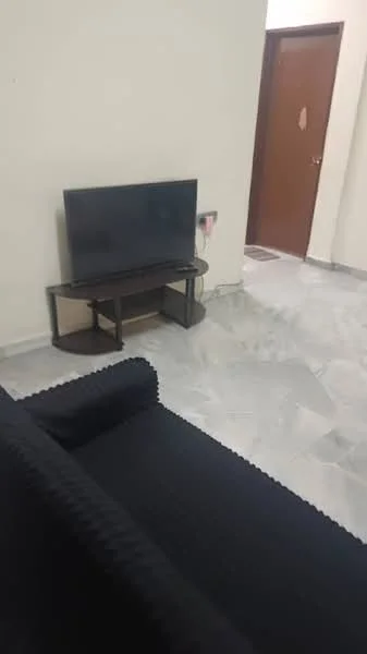 Living features: black fabric sofa, wooden TV console, flat-screen TV, marble flooring, light beige painted walls, wooden door, wall-mounted electrical outlet.