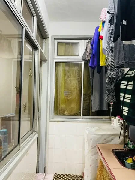 Laundry features: window with glass panes, white tiled walls, white tiled flooring, clothes hanging on a rack, sink, countertop, laundry basket, shelf with cleaning supplies.