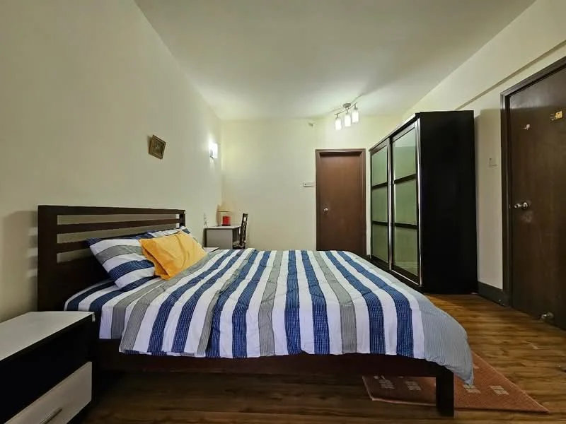Bedroom features: queen-size bed with striped bedding, wooden bed frame, nightstand with drawer, black wardrobe with sliding doors, wooden flooring, wall-mounted lights, study desk with chair, door leading to hallway; style: modern.