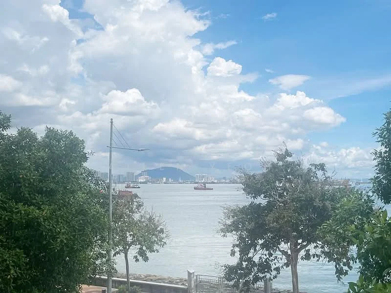 Exterior features: waterfront view, city skyline in background, trees in foreground, cloudy sky, boats on water, hills in distance.