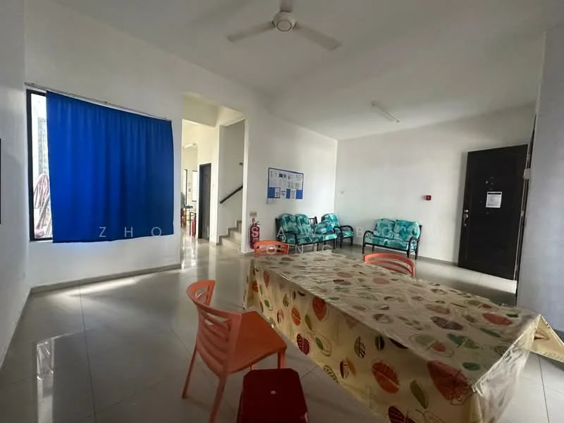 Living features: white painted walls, glossy tile flooring, ceiling fan, large window with blue curtain, dining table with patterned tablecloth, plastic chairs in orange, green patterned chairs, fire extinguisher on wall, door to hallway, wall-mounted notice board.