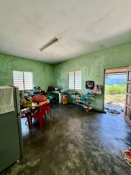 Kitchen features: green painted walls, concrete flooring, two windows, wooden door, table with red plastic chairs, kitchen cabinets, sink, refrigerator, stove, countertop, various kitchen utensils, open space leading outside; view: garden.