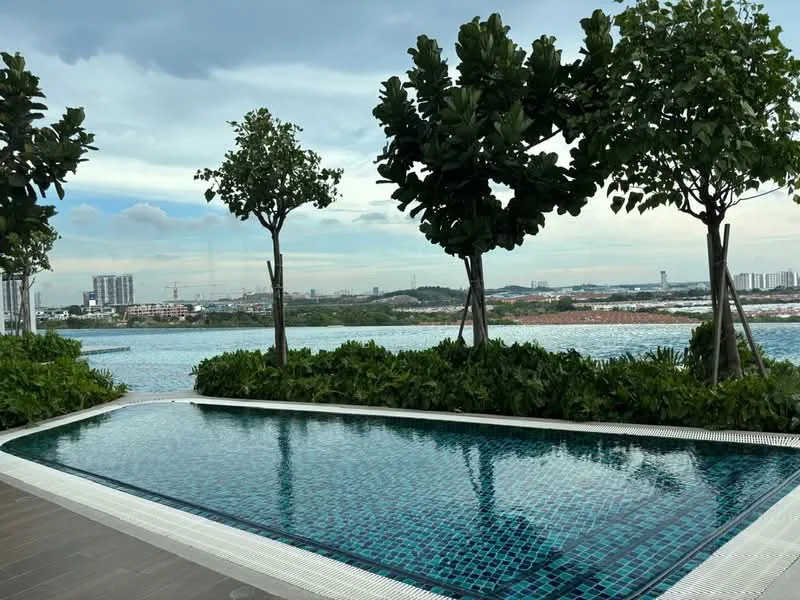 Exterior type: swimming pool deck; features: infinity pool, tiled pool with mosaic pattern, surrounded by tropical landscaping, manicured greenery, trees providing shade, city skyline view in background; style: modern.