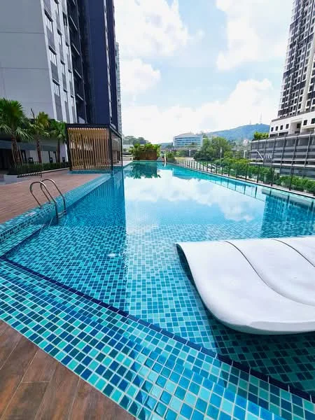Exterior type: swimming pool deck; features: infinity pool, tiled pool deck with mosaic tiles, poolside loungers, landscaped greenery surrounding the pool, wooden decking area, view of city skyline in background, sunny weather with clear blue sky; style: modern.