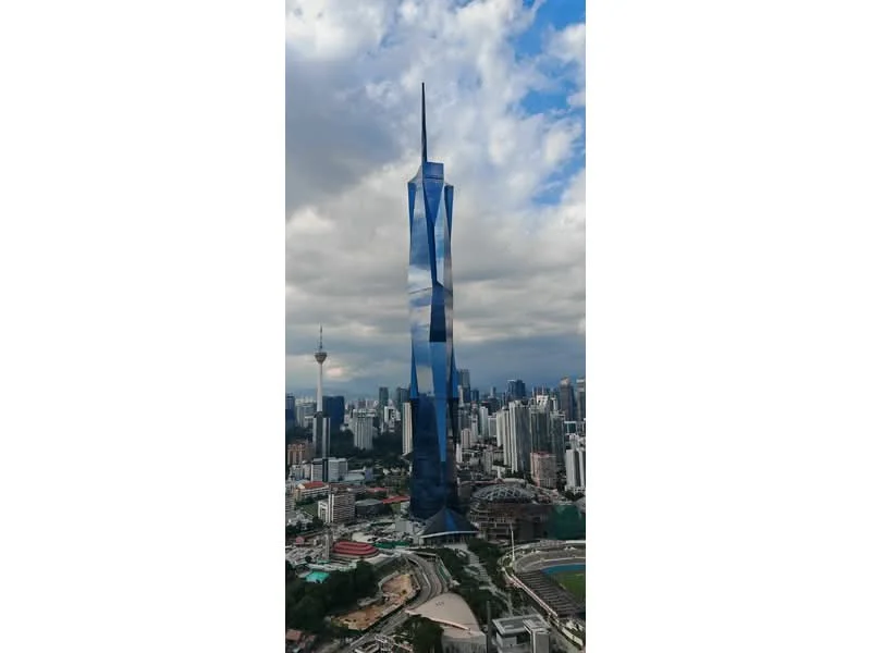 Exterior type: high-rise condominium; features: glass curtain wall, blue reflective facade, sharp spire, surrounded by urban landscape, adjacent to green spaces, visible city skyline in background; style: modern.