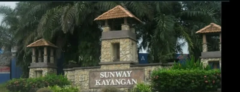 Exterior type: main entrance gate; features: stone-clad entrance structure, two decorative towers, thatched roof on towers, wooden signage with 'SUNWAY KAYANGAN', landscaped greenery, palm trees, flowering plants, manicured bushes; style: tropical-modern.