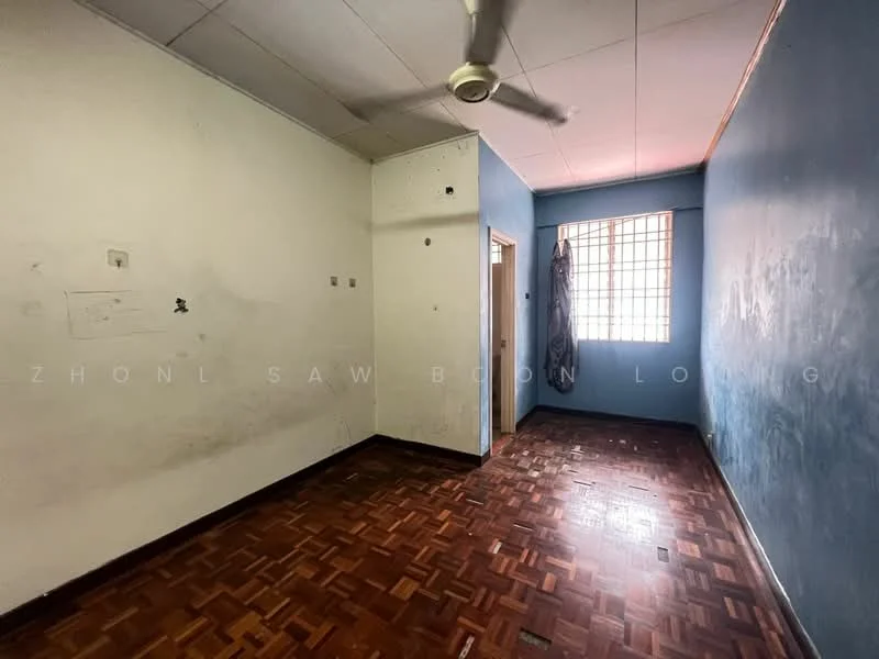 Room features: blue painted walls, wooden parquet flooring, ceiling fan, window with metal grille, door leading to another room, unpainted wall section, natural light from window.
