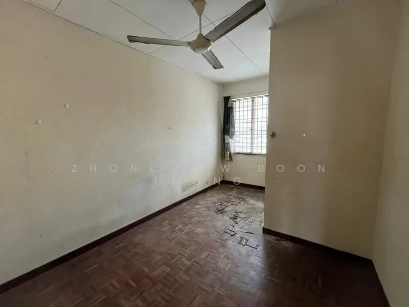 Room features: parquet wood flooring, white painted walls, ceiling fan, window with metal grille, curtains, corner with visible wall damage, no visible furniture or decor.