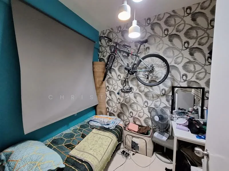 Bedroom features: single bed with patterned bedding, decorative throw blanket, wall-mounted bicycle, floral wallpaper, blue accent wall, ceiling light fixtures, mirror on dresser, fan on floor, small dresser with personal items, curtain for window; style: modern.