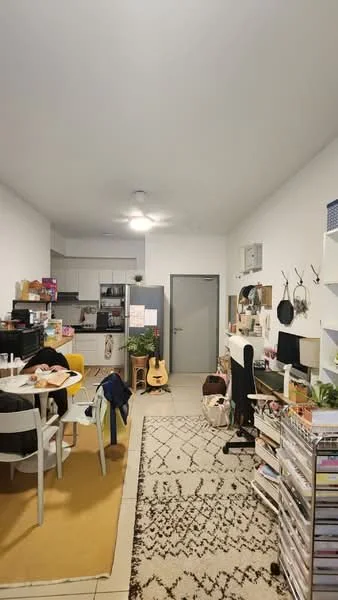 Room features: white painted walls, grey ceiling, tile flooring, area rug with geometric pattern, round dining table, 4 dining chairs, black piano, guitar, open shelving unit, desk with chair, kitchen area visible in background, refrigerator, kitchen cabinets, countertop, wall-mounted air conditioning unit; style: modern.